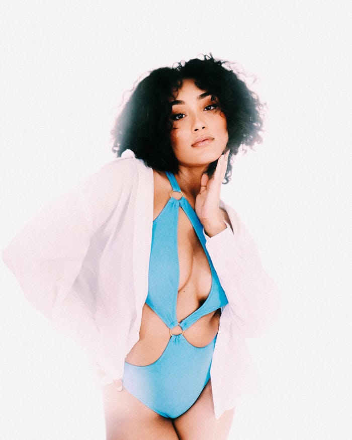 A fashionable young woman in blue swimwear poses confidently against a bright backdrop.